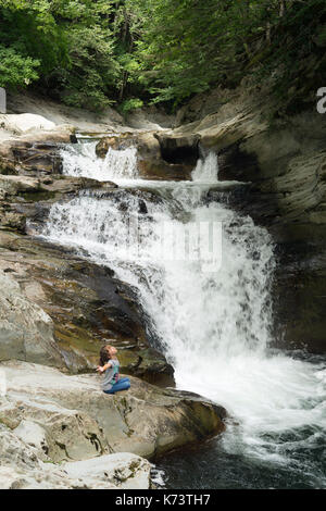 Mädchen sitzt auf einem Felsen neben den Wasserfall von der Schaufel in die Selva de Irati in Navarra, Spanien. Stockfoto