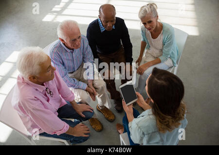 Hohe Betrachtungswinkel der weiblichen Lehrer holding Tablet beim Sitzen mit älteren Menschen während der Diskussion im Kunstunterricht Stockfoto