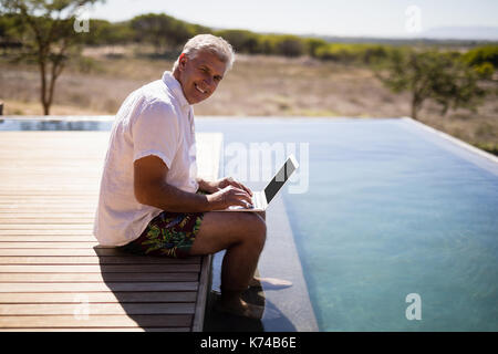 Portrait von lächelnden Mann mit Laptop in der Nähe der Pool während der Safari Ferienhäuser Stockfoto