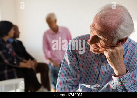 Nachdenklich älterer Mann mit Freunden im Hintergrund bei Kunst Klasse Stockfoto