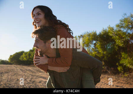 Glückliche junge Mann, Frau, Huckepack Fahrt auf Feld Stockfoto