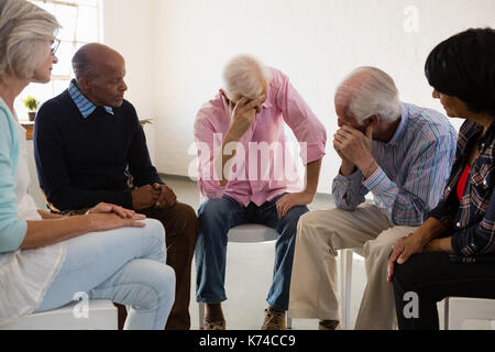 Ältere Freunde auf der Suche nach Mann mit dem Kopf in der Hand sitzen auf Stuhl im Kunstunterricht Stockfoto