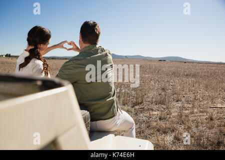 Ansicht der Rückseite des jungen Paares, Herzform mit den Händen auf Off Road Fahrzeug mit Landschaft Stockfoto