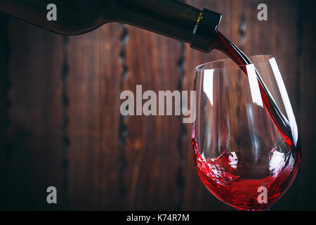 Gießen Rotwein ins Glas auf Holz- Hintergrund Stockfoto