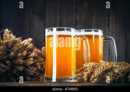 Zwei Gläser helles Bier mit ährchen von Gerste auf dem hölzernen Hintergrund. Schönen Hintergrund des Oktoberfestes Stockfoto