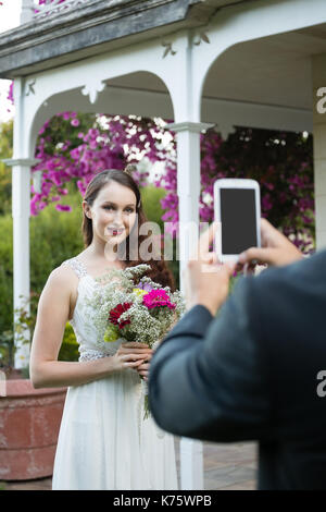 7/8 die Hände des Bräutigams fotografieren Braut holding Blumenstrauß im Park Stockfoto