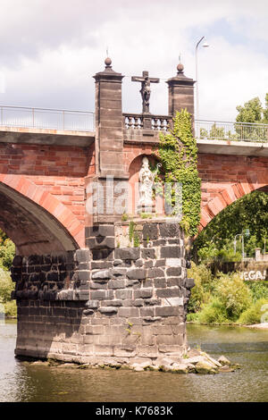 TRIER, Deutschland - 4. Aug. 17: ein römisches Kruzifix mit der Statue einer Papst auf der Römerbrücke mit Blick auf die Mosel. Stockfoto