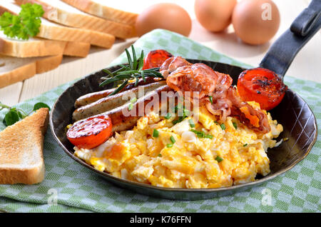 Rührei mit gebratenem Speck und Würstchen in der Pfanne serviert. Stockfoto