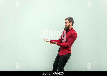 Bärtiger Mann in lässiger Kleidung, hält etwas schwer. Studio-Aufnahme, grauer Hintergrund Stockfoto