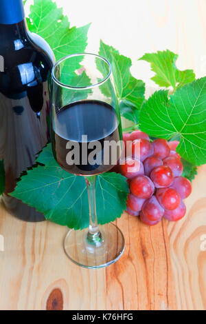 Flasche Rotwein mit Glas und Trauben auf Holz. Stockfoto