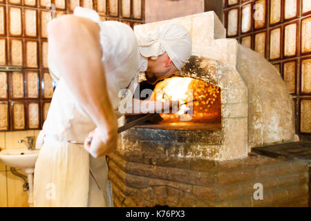 Die Rückansicht der Herd in die weiße Uniform, Pizza in den brennenden Brennofen im Restaurant. Stockfoto