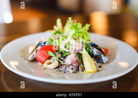 Die seitliche Ansicht der Salat von Meeresfrüchten wie Muscheln, Tintenfische, Salat, Tomaten, Zitronen- und Zwiebel Kreise auf dem weißen Teller platziert. Stockfoto