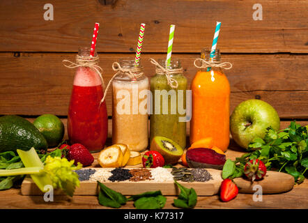 Auswahl an Obst und Gemüse-Smoothies in Glasflaschen mit einem Strohhalm auf hölzernen Hintergrund. Stockfoto