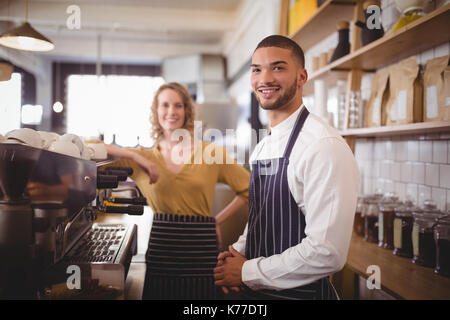 Portrait von lächelnden jungen Kellner und Kellnerinnen stehen durch die espressomaschine im Coffee Shop Stockfoto