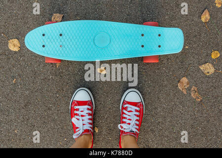 Bis der Füße eines Mädchens in rote Turnschuhe und Blue Penny Skate Board mit rosa Räder schließen. städtischen Szene, Leben in der Stadt. Sport, Fitness Lifestyle. Stockfoto