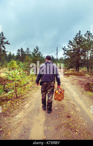 Der Mensch kommt mit einem Korb von Pilzen auf der Straße. Herbst Wald. Stockfoto