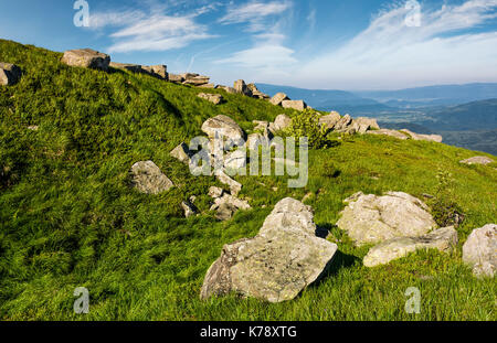 Riesige Felsbrocken auf einem grasigen Hang in den Bergen. schöne Berglandschaft mit Himmel voller Wolken Stockfoto