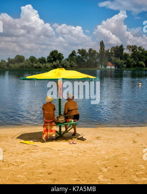 Frauen auf dem Village am Strand unter einem gelben Sonnenschirm. Riverside Stockfoto