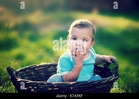 Eine junge baby boy in einem Weidenkorb hocken und essen Brot Stockfoto