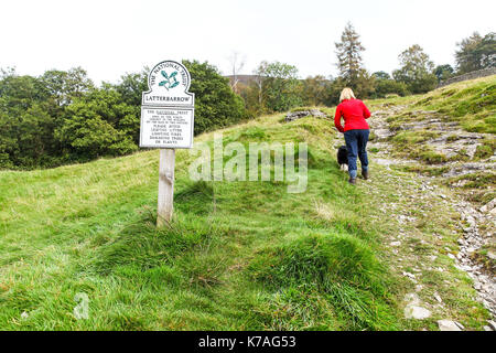 Eine Frau mit ihrem Hund hinter einem National Trust Omega Schild Latterbarrow, Lake District, Cumbria, England, Großbritannien Stockfoto