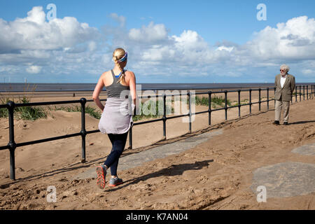 Crosby, Merseyside. 15 Sep, 2017. UK Wetter. Sonnig, aber breezy Tag an der Küste auf die Seemänner, die Art und Weise. Die lange Promenade von Crosby, Formby, ist mit Wind abgedeckt - Sand, die Jogger, die Übung auf der Esplanade geblasen. Credit: MediaWorldImages/Alamy leben Nachrichten Stockfoto