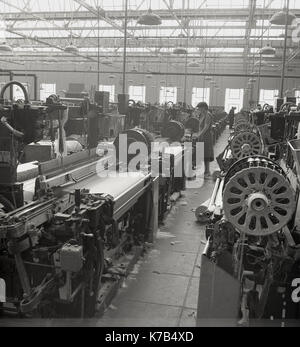 In den 1950er Jahren standen historische Arbeiterinnen auf Holzdielen mit mechanisierten Leinenwebstühlen in einer großen Textilfabrik in Nordirland. Stockfoto
