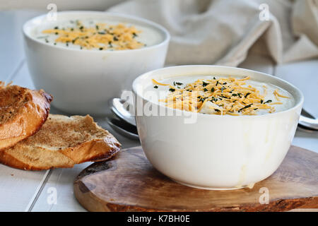 Heiße Kartoffelsuppe mit Sauerrahm, Cheddar Käse und Schnittlauch mit in Scheiben geschnittenen, geröstetes Brot. Extrem flache Tiefenschärfe mit selektiven Fokus auf Schüssel in Stockfoto