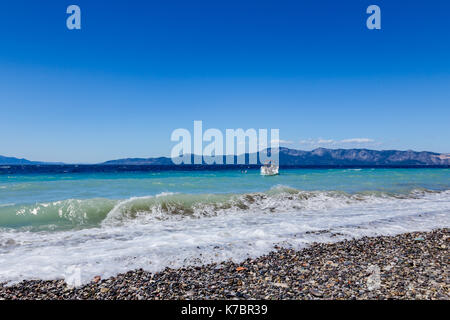 Wellen an der Küste, Meer mit schäumenden Wellen mit kleinen Boot auf dem Wasser im Hintergrund. Stockfoto