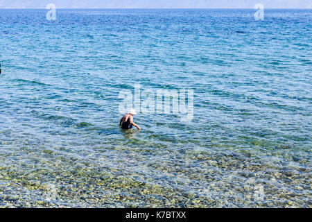 Frau wird in seichten Meer Wasser in Badeanzug mit weißen Hut auf dem Kopf. Stockfoto