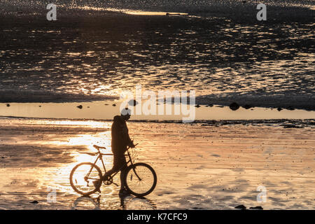 Ein einsamer Radfahrer hält am Strand, um den Sonnenuntergang zu bewundern. Stockfoto
