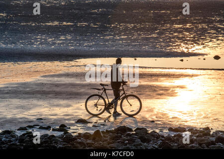 Ein einsamer Radfahrer hält am Strand, um den Sonnenuntergang zu bewundern. Stockfoto