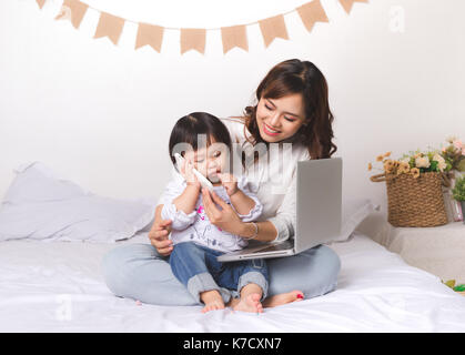 Asiatische Dame im klassischen suitvworking auf Laptop zu Hause mit Ihrem Baby Mädchen chatten mit Vater. Stockfoto