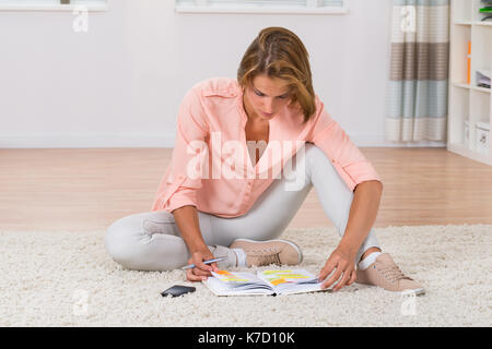 Junge Frau schreiben Hinweis im Tagebuch während der Sitzung auf dem Teppich Stockfoto