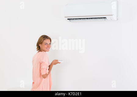 Junge Frau, die Klimaanlage mit Fernbedienung Stockfoto