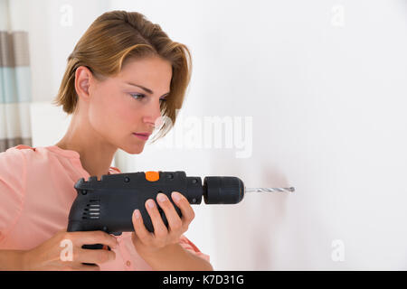 Porträt der jungen Frau, die das Loch in der Wand mit Bohrmaschine Stockfoto