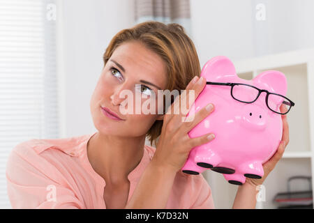 Foto der jungen schönen Frau Schütteln Sparschwein Stockfoto