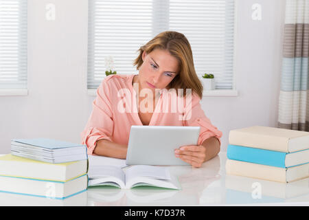 Junge Frau mit Büchern über digitale Tablet am Schreibtisch Stockfoto