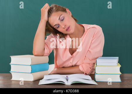 Müde junge Lehrerin mit Bücher am Schreibtisch im Klassenzimmer Stockfoto