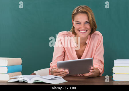 Junge gerne Lehrerin mit Büchern und digitalen Tablette im Klassenzimmer Stockfoto