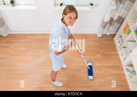 Junge weibliche Hausmeister wischen Holzboden im Haus Stockfoto