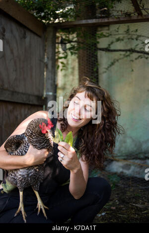 Glückliche Frau füttern Blätter zu Huhn, während sich in Geflügelfarm Stockfoto