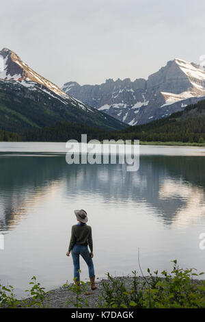 Ansicht der Rückseite des weiblichen Wanderer in Aussicht beim Stehen auf Ufer durch Swiftcurrent Lake Stockfoto