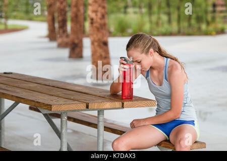 Jugendmädchen ruhender Kopf über Wasser Flasche beim Sitzen auf der Werkbank Stockfoto