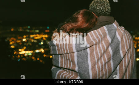 Ansicht der Rückseite des jungen Paares in einer Decke gegen Stadtbild bei Nacht gewickelt Stockfoto