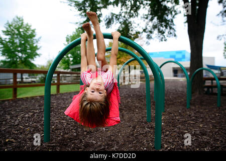 Portrait von Mädchen hing kopfüber an outdoor Spielgeräte am Spielplatz Stockfoto