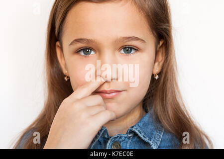 Kleines Kindermädchen, Das Seine Nase Auf weißem Hintergrund Pflückt und Camera Close-up betrachtet. Stockfoto