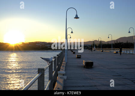 Goldene stunde Australien. Sonnenuntergang gesehen von Jetty in Coffs Harbour, Urlaub, Australien. Menschen zu Fuß Straße Lampen, Holzbank, etc. Stockfoto