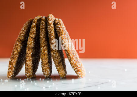 Snap Ginger Spice Cookies mit Zucker Kristalle. Weißer Marmor Zähler nach oben. Dark orange hinterlegt. Auf der Seite stapeln. Stockfoto