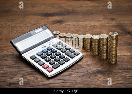 Close-up Taschenrechner mit Stapel von Münzen auf hölzernen Tisch Stockfoto