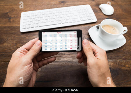 Nahaufnahme der Person Hände mit Handy Übersicht Kalender auf Schreibtisch Stockfoto